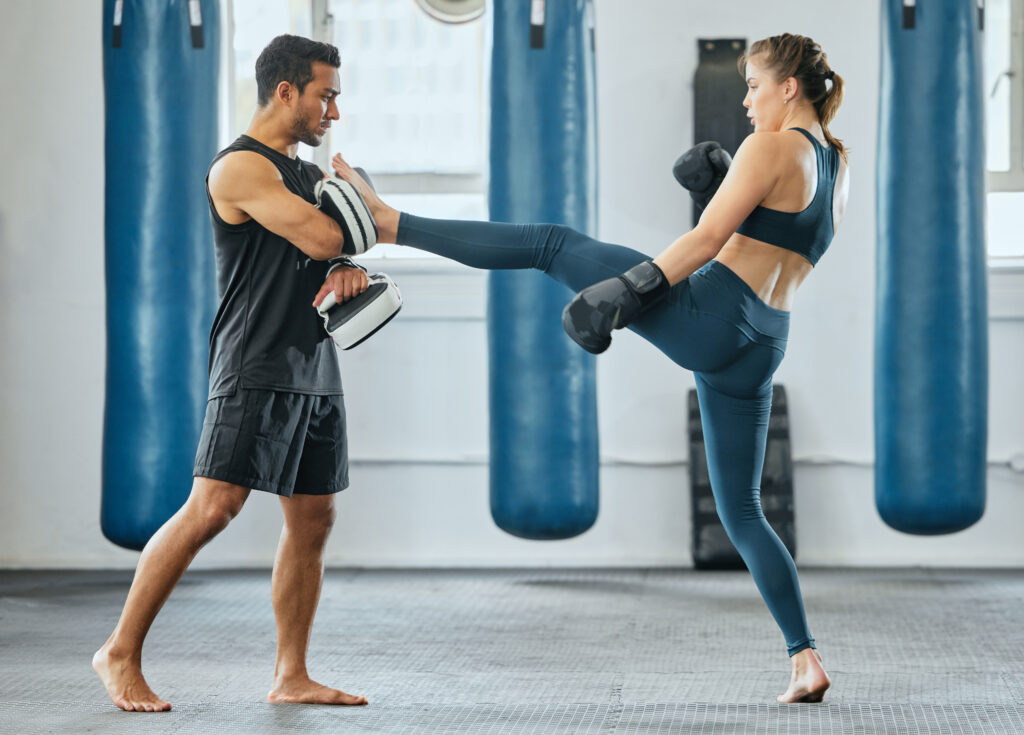 Training krav maga and learning to fight, a male trainer and woman getting fit in gym. Fitness, motivation and female empowerment. Strong kick and healthy exercise, a young lady and her sports coach.